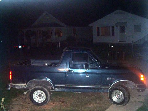 1988 Ford Bronco - Side view of a dark blue SUV with a removable top, parked at night in front of houses.