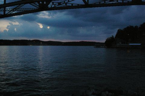 1998 Jeep TJ - A lake scene unfolds under a large bridge as dusk settles, with the Supermotors logo visible in the corner.