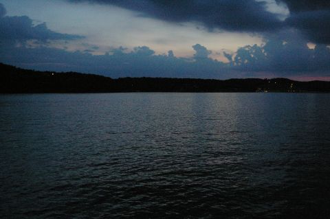 1998 Jeep TJ - A wide shot of a lake at dusk, with a dark, tree-covered shoreline in the distance and dramatic clouds overhead.