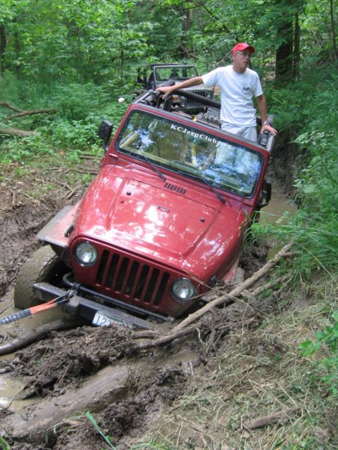 1998 Jeep TJ - A red Jeep Wrangler TJ is stuck in a muddy trail, with another Jeep visible behind it.