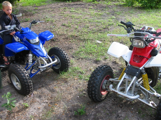 Blue Yamaha ATV and red/white ATV parked on grass, child on blue quad