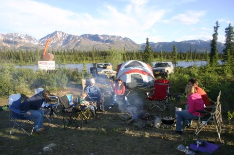 2003 Jeep TJ - Campers gather around a fire with tents and vehicles at a scenic mountain lake location.