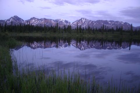 2003 Jeep TJ - A mountain range and forest are mirrored in the still waters of a lake under a cloudy sky.