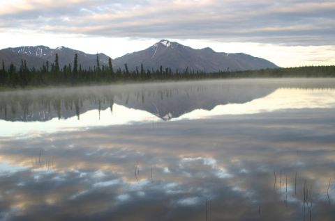 2003 Jeep TJ - A misty lake reflects mountains and trees under a cloudy sky, creating a tranquil natural scene.