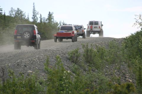 2003 Jeep TJ - A convoy of SUVs and a van travels along a dusty gravel road, kicking up dust in their wake.