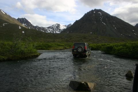 2003 Jeep TJ - A black SUV navigates a river in a mountainous, brush-covered landscape.