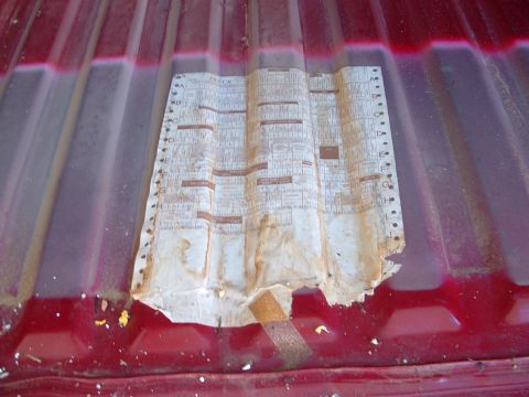1990 Ford Bronco - A crumpled document with printed text lies on the ribbed surface of a red vehicle bed.