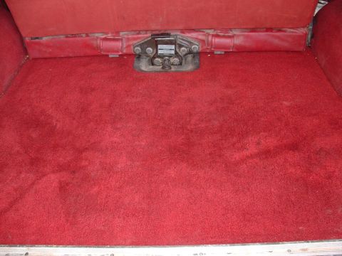1990 Ford Bronco - The rear cargo area of a vehicle is shown with red carpeting and a central latch mechanism.