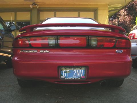 1996 Ford Probe - The rear of a red 1996 Ford Probe is shown parked in front of a garage, with another vehicle to its left and right.