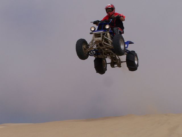 Blue ATV mid-air jump, rider in red helmet and shirt