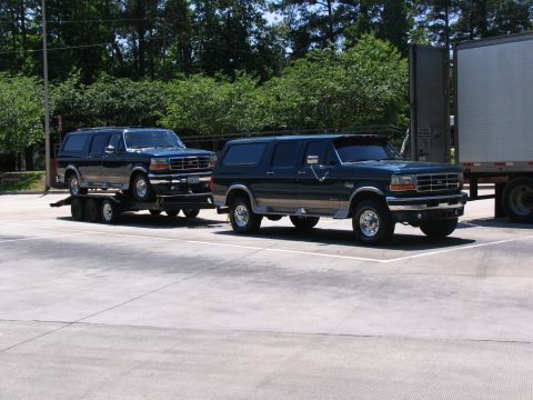 1978 Ford Bronco - Two dark green Ford Bronco SUVs are parked side-by-side, with one loaded onto a trailer.