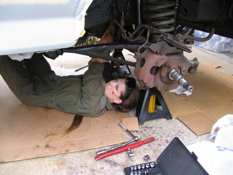 1978 Ford Bronco - A person in overalls works on the suspension of a vehicle supported by jack stands.
