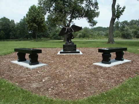2001 Mercury Grand Marquis - A memorial statue stands in a park, flanked by benches, with trees and a grassy field in the background.
