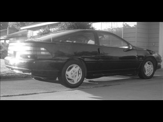 1991 Ford Probe - A black 1991 Ford Probe is seen from the rear quarter angle, parked in front of a building.