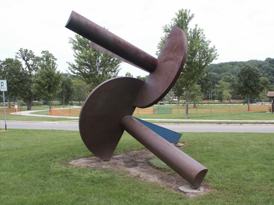 Abstract metal sculpture in a park setting with a parking sign