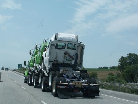 2001 Mercury Grand Marquis - Several trucks are being transported on a highway, loaded onto a larger transport truck.