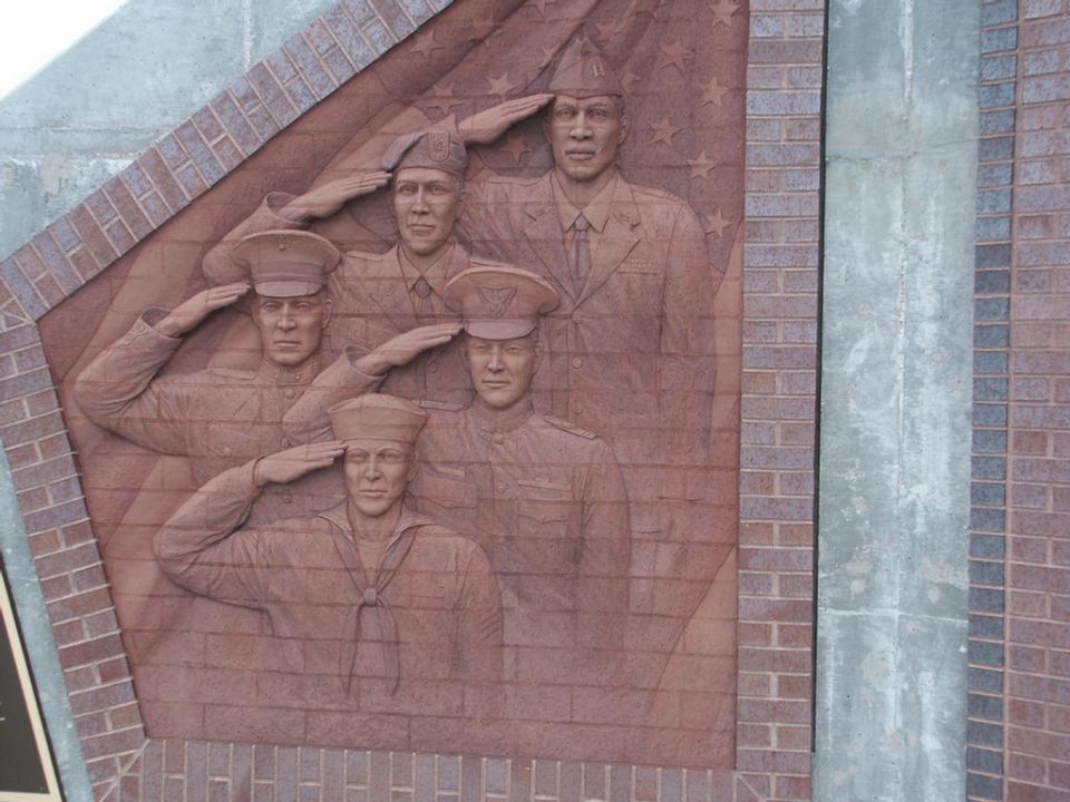 Relief sculpture of four soldiers in uniform saluting, set against a brick wall