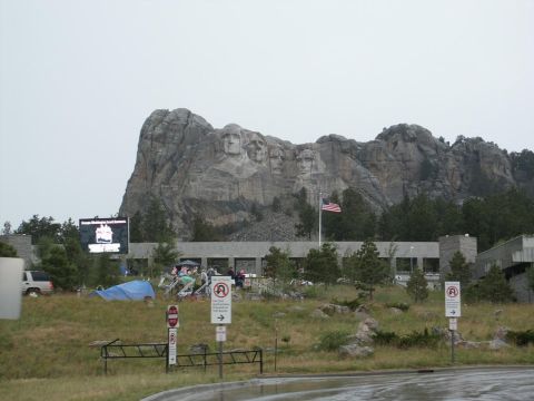 2001 Mercury Grand Marquis - A white SUV is visible near the entrance to Mount Rushmore National Memorial, with a large screen displaying an advertisement.