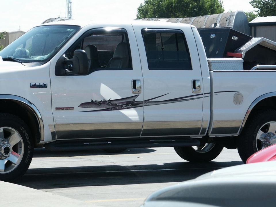 White Ford F-250 Super Duty pickup truck, side view, showing F-250 badge and a tribal graphic. Another vehicle is partially visible in the foreground