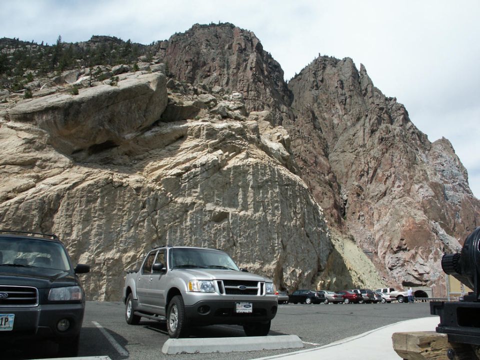 Silver Ford Explorer Sport Trac pickup truck parked in a lot with a rocky mountain behind it. Another SUV is parked to its left