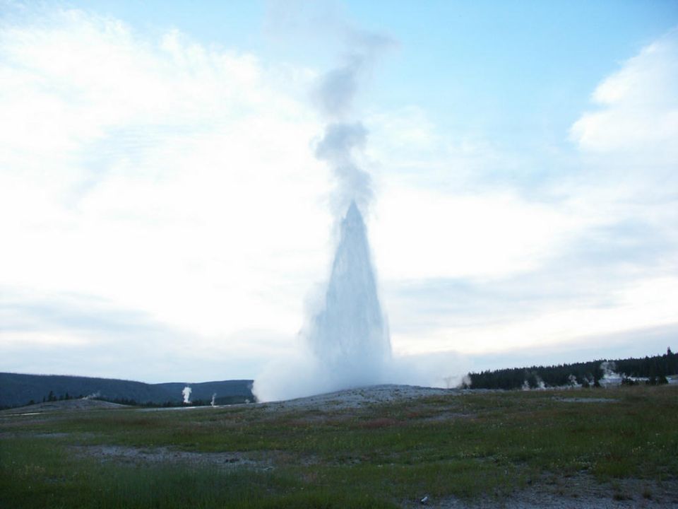 Old Faithful geyser erupting with steam and water shooting high into the sky against a blue sky with clouds