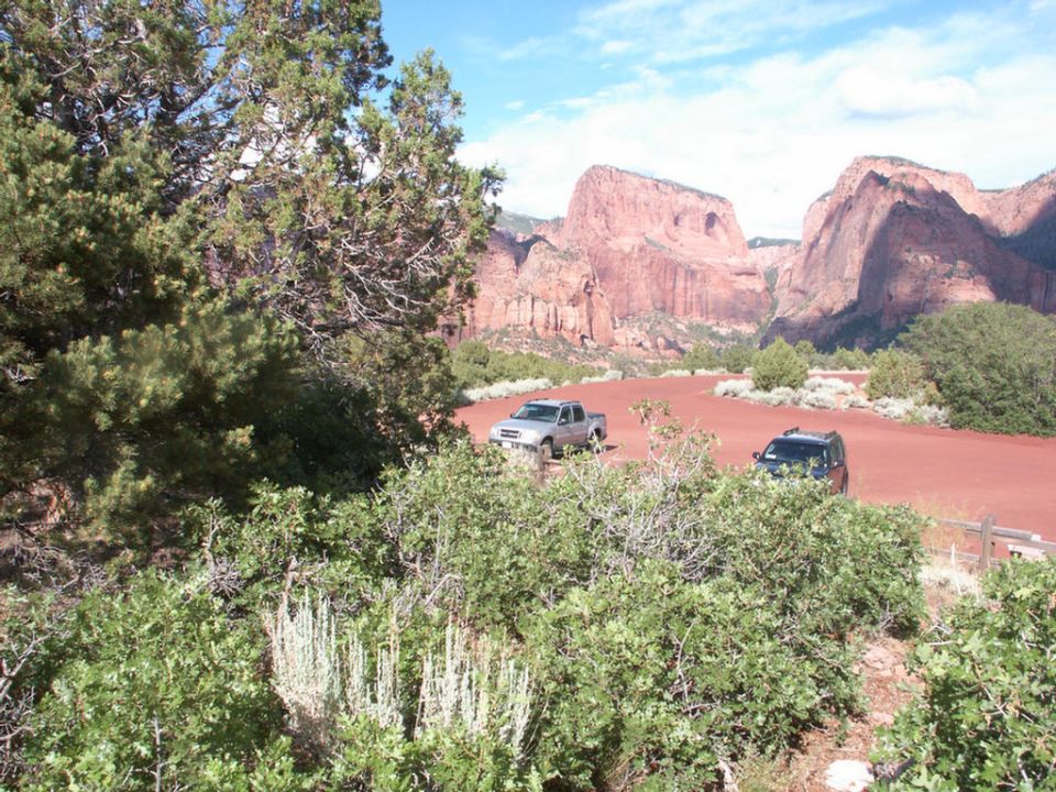 Silver pickup truck and dark SUV parked on a dirt lot with red rock formations in the background
