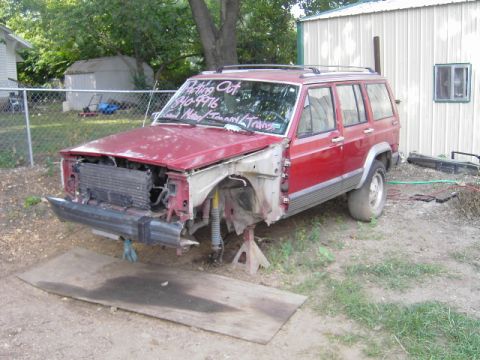 1991 Jeep Cherokee - A red 1991 Jeep Cherokee sits in a yard with its front bumper and grille missing.