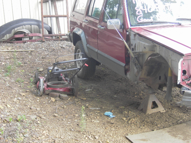 Red Jeep Cherokee with front end removed, jack stands, lawnmower