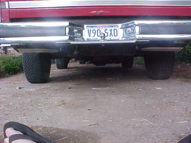 Rear low-angle view of maroon vehicle with chrome bumper, Texas plate V90 SXD, and dual exhaust tips
