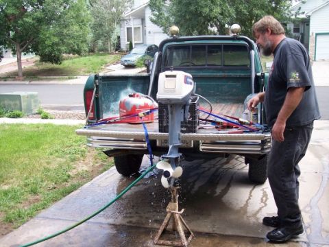 1972 Ford Ranchero - A man stands by the tailgate of a green pickup truck, which is loaded with a boat motor and a red gas can.