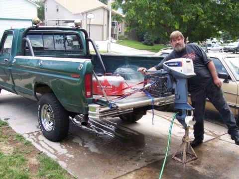 1972 Ford Ranchero - A man stands by a green pickup truck, preparing an outboard motor that is mounted on a stand.