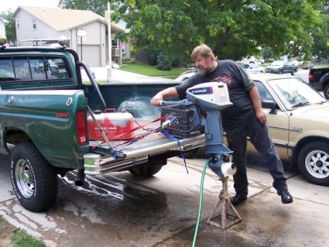 1972 Ford Ranchero - A man prepares an outboard motor next to a green pickup truck, with another vehicle visible in the background.