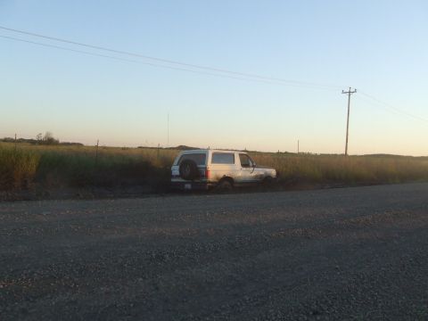 1990 Ford Bronco - A white SUV is stuck in the mud next to a dirt road with a telephone pole in the background.