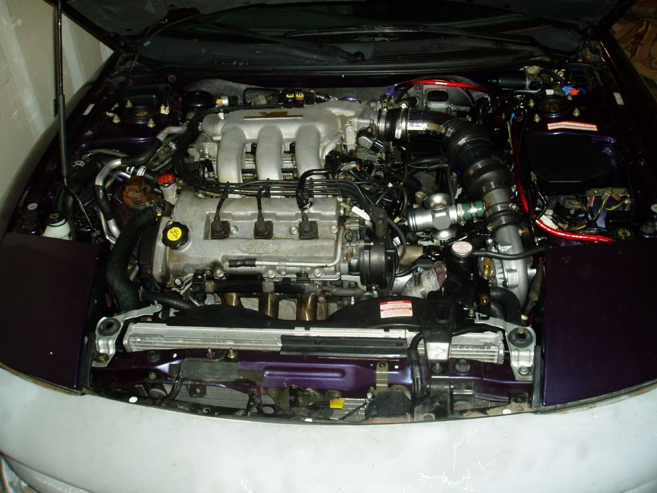 Engine bay of a purple car with the hood open. Shows the V6 engine, intake, and radiator