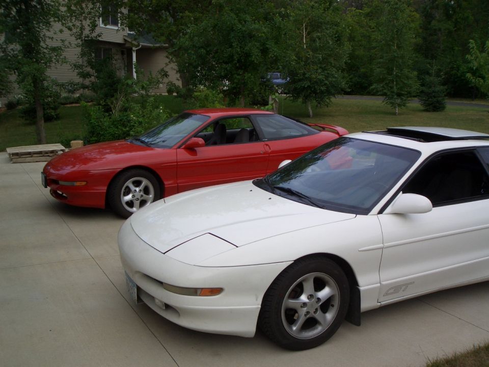 Red Ford Probe coupe and white Ford Probe GT parked on a driveway near trees