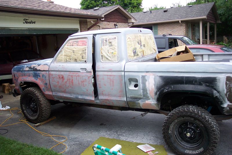 Primer-gray extended-cab Ford Ranger with newspaper-masked windows and mud tires, prepped for paint in a driveway