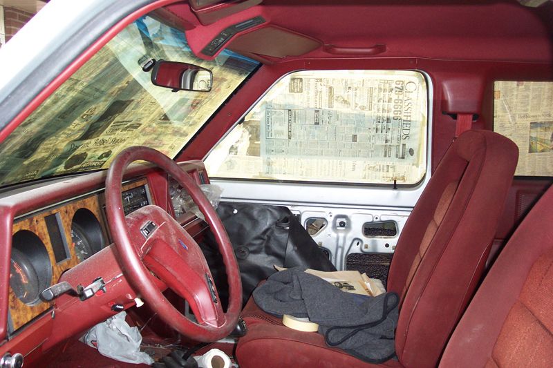 Red truck interior with newspaper-masked windows, bare door panel, and painting supplies on the seat