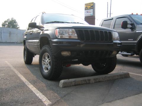 2005 Ford F-250 - A dark colored Jeep Grand Cherokee is parked in a parking lot, with a large pickup truck visible to its right.