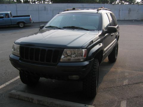2005 Ford F-250 - A dark green Jeep Grand Cherokee is parked in a lot, with a blue pickup truck in the background.