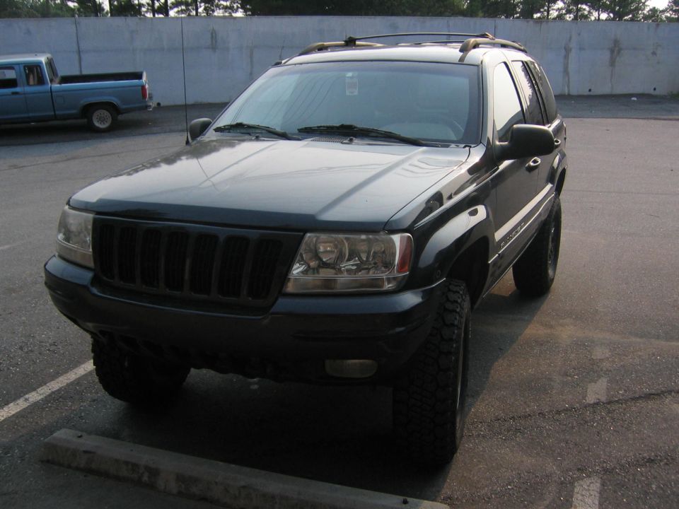 Dark green Jeep Grand Cherokee with aftermarket grille and tires, parked at an angle