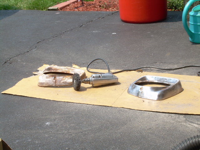 Two vintage truck headlight bezels on cardboard with a wire-brush grinder mid-stripping