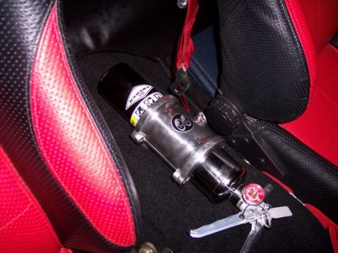 1972 Ford Ranchero - A fire extinguisher is mounted between the seats of a vehicle with red and black perforated upholstery.