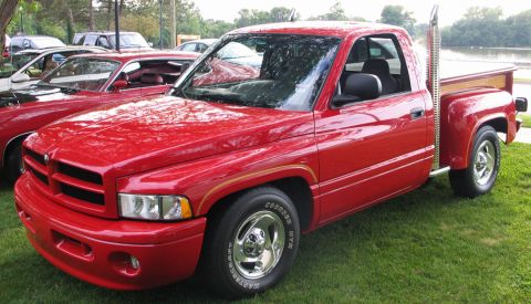 1994 Ford Bronco - A red pickup truck with a prominent chrome exhaust stack is parked on a grassy area next to other vehicles.
