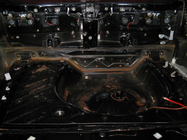 Stripped trunk interior with bare spare tire well, exposed taillight wiring and black sheet metal