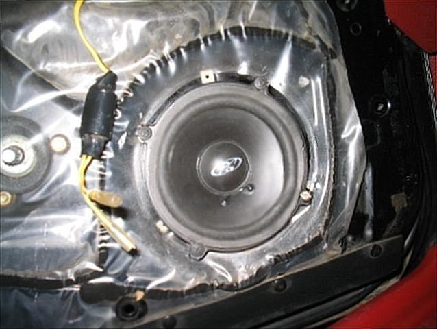 Ford door speaker mounted behind plastic vapor barrier inside a vehicle door panel