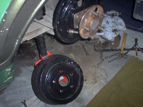 1970 Ford Ranchero - A removed brake drum rests on a jack next to the hub assembly, with tools scattered on the garage floor.