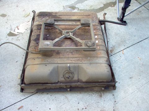 1970 Ford Ranchero - A used vehicle fuel tank with visible rust and a metal support bracket is shown on a concrete surface.