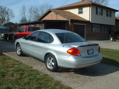 2002 Ford Taurus - A silver 2002 Ford Taurus is parked in front of a house with a red truck visible in the background.