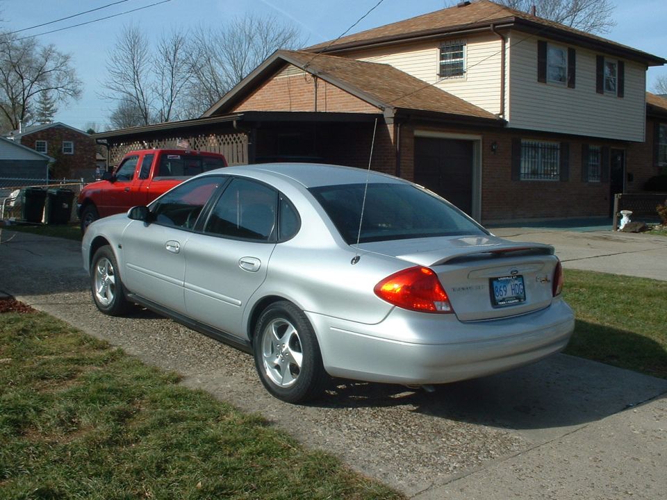 Silver sedan rear three-quarter view in a driveway with black lip spoiler and alloy wheels