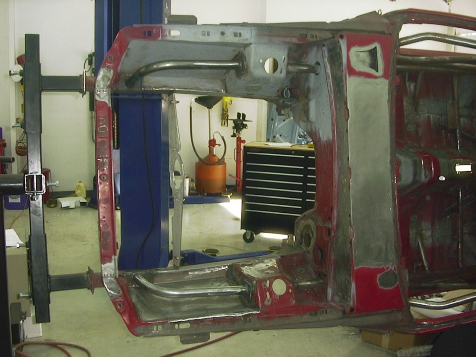 Car frame undergoing restoration on a lift, showing structural components and bare metal